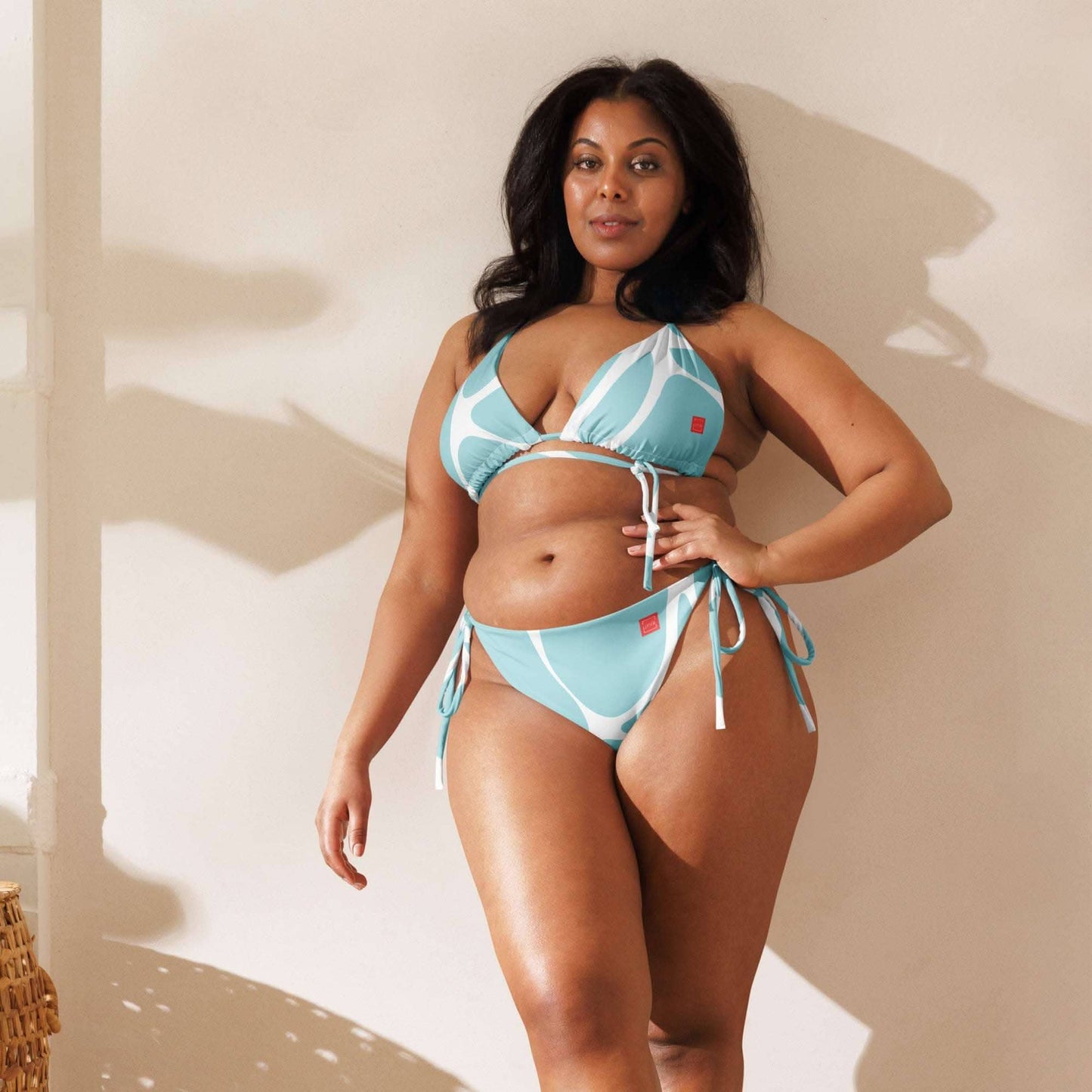 Curvy woman wearing a blue and white ethical fashion bikini by unik fashion standing against a beige wall