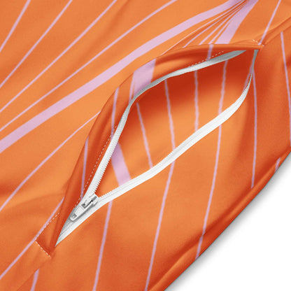 Close-up of orange sustainable track jacket pocket with white zipper and pink stripe details