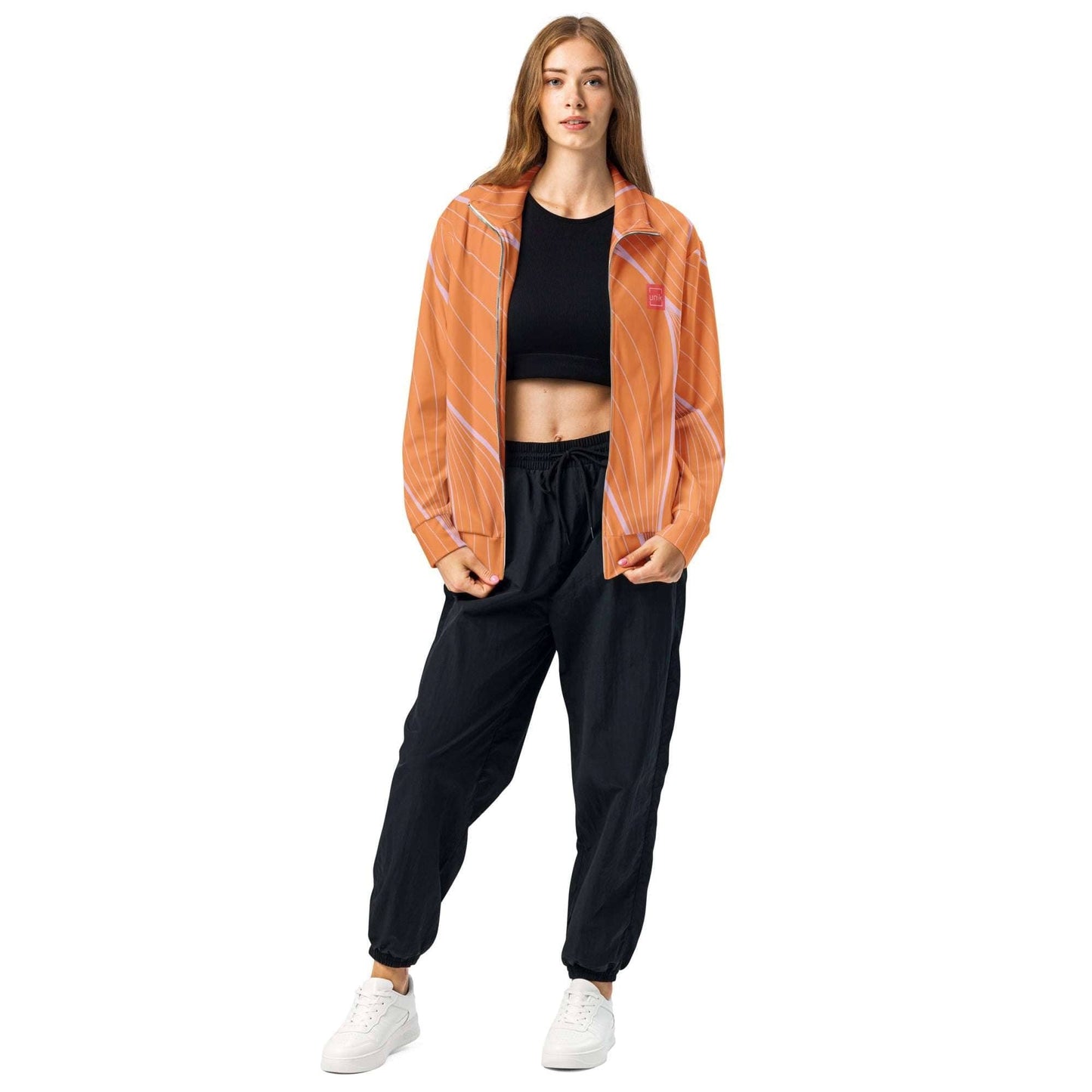 Woman wearing an orange sustainable track jacket with black pants and white sneakers